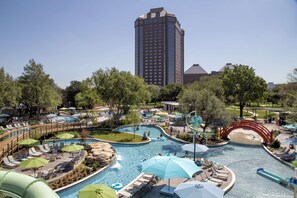 A resort with a large swimming pool, lounge areas, and a tall building in the background.