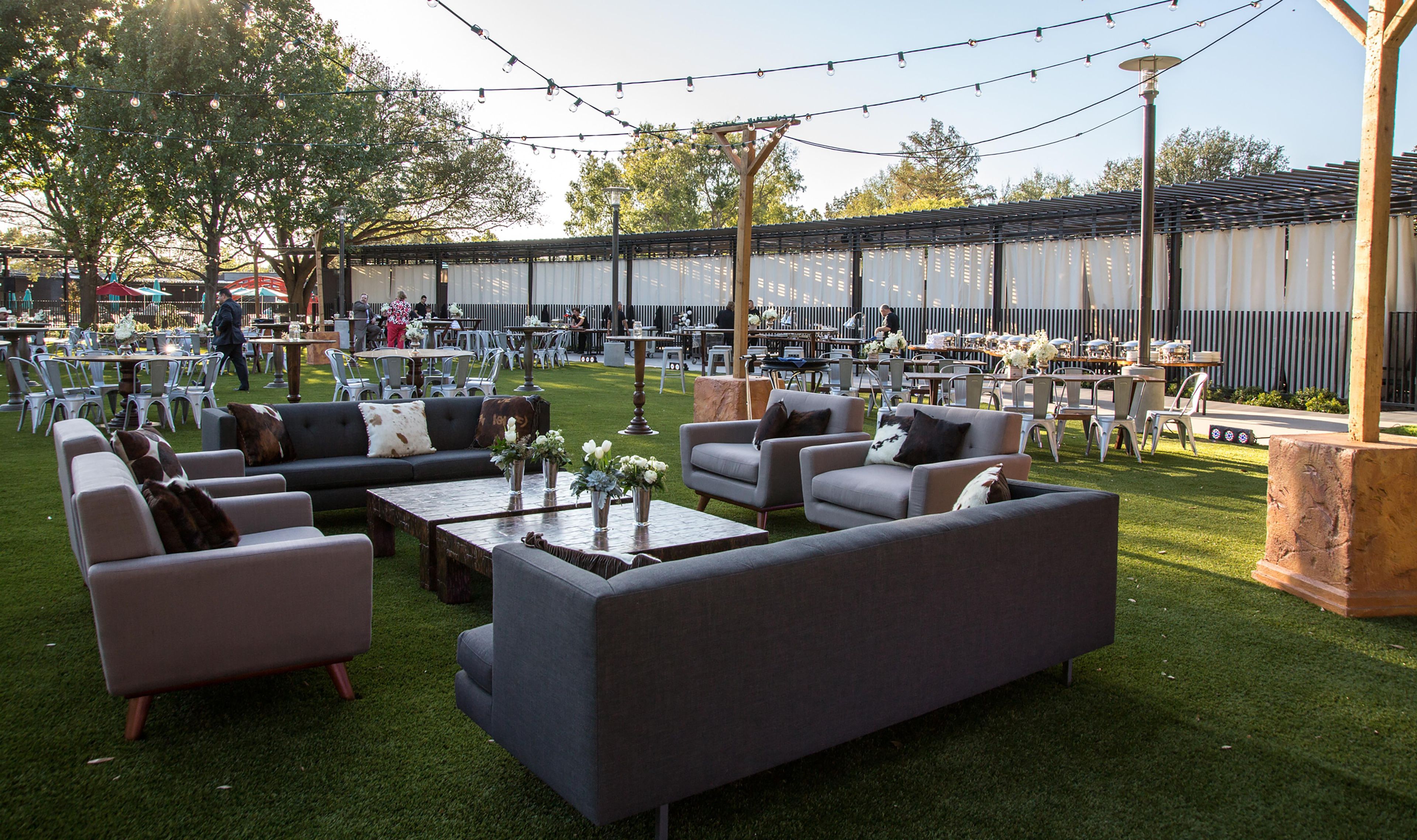 An outdoor seating area with sofas and tables, surrounded by a covered patio and string lights.