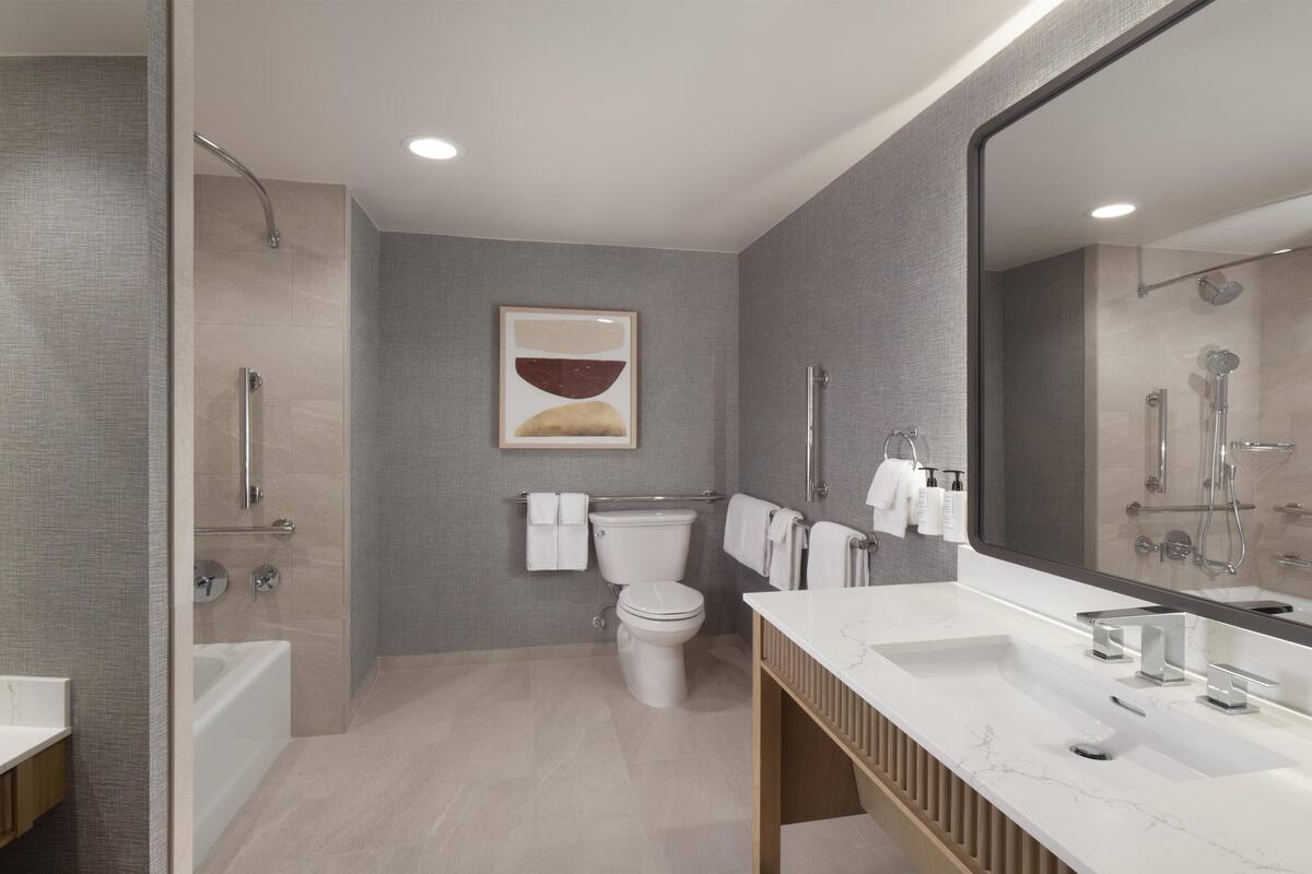 A modern bathroom with a bathtub, toilet, and sink, featuring a large mirror and a shower.