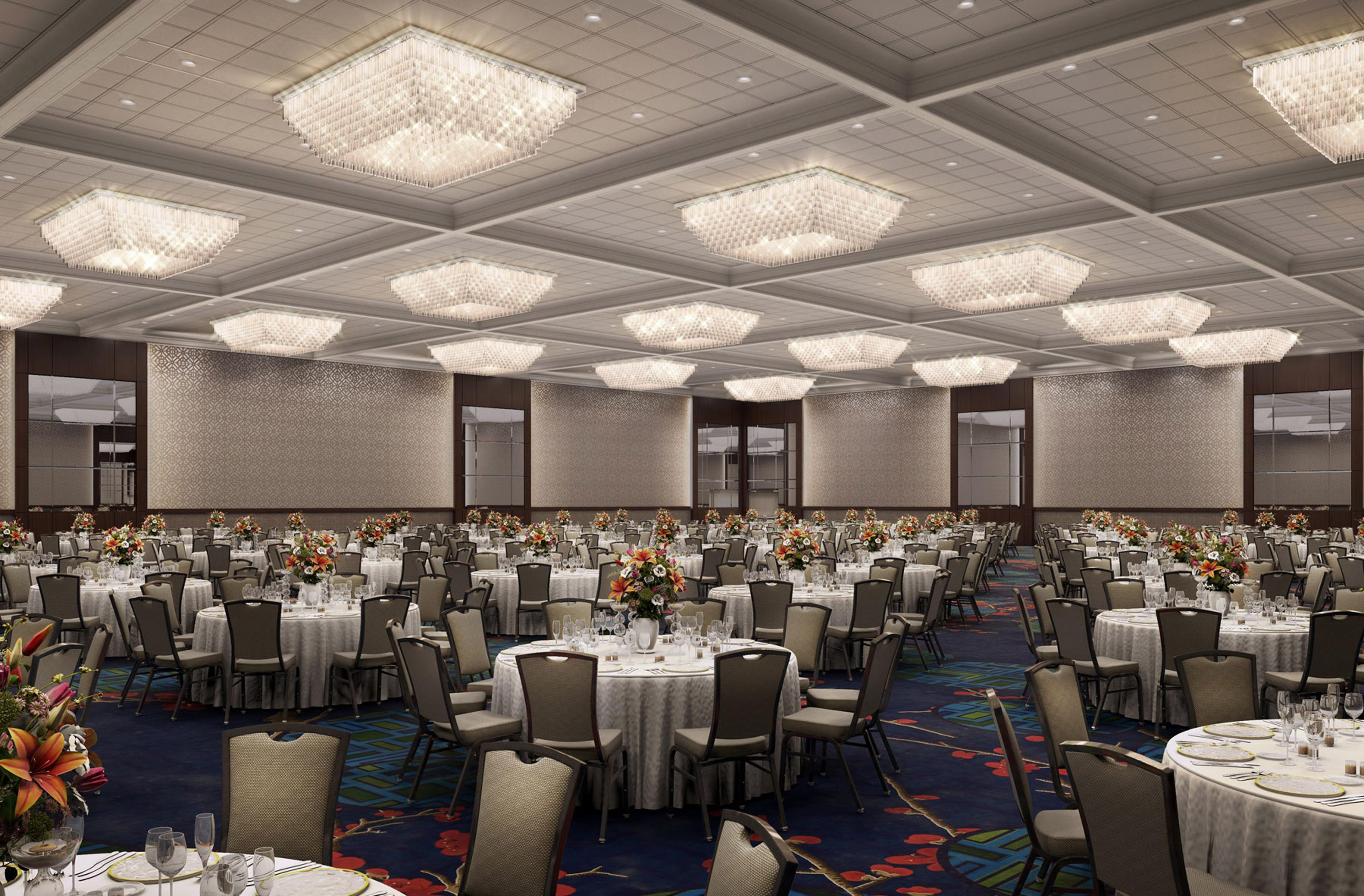 A large banquet hall with multiple round tables, each set with white tablecloths, chairs, and floral centerpieces.