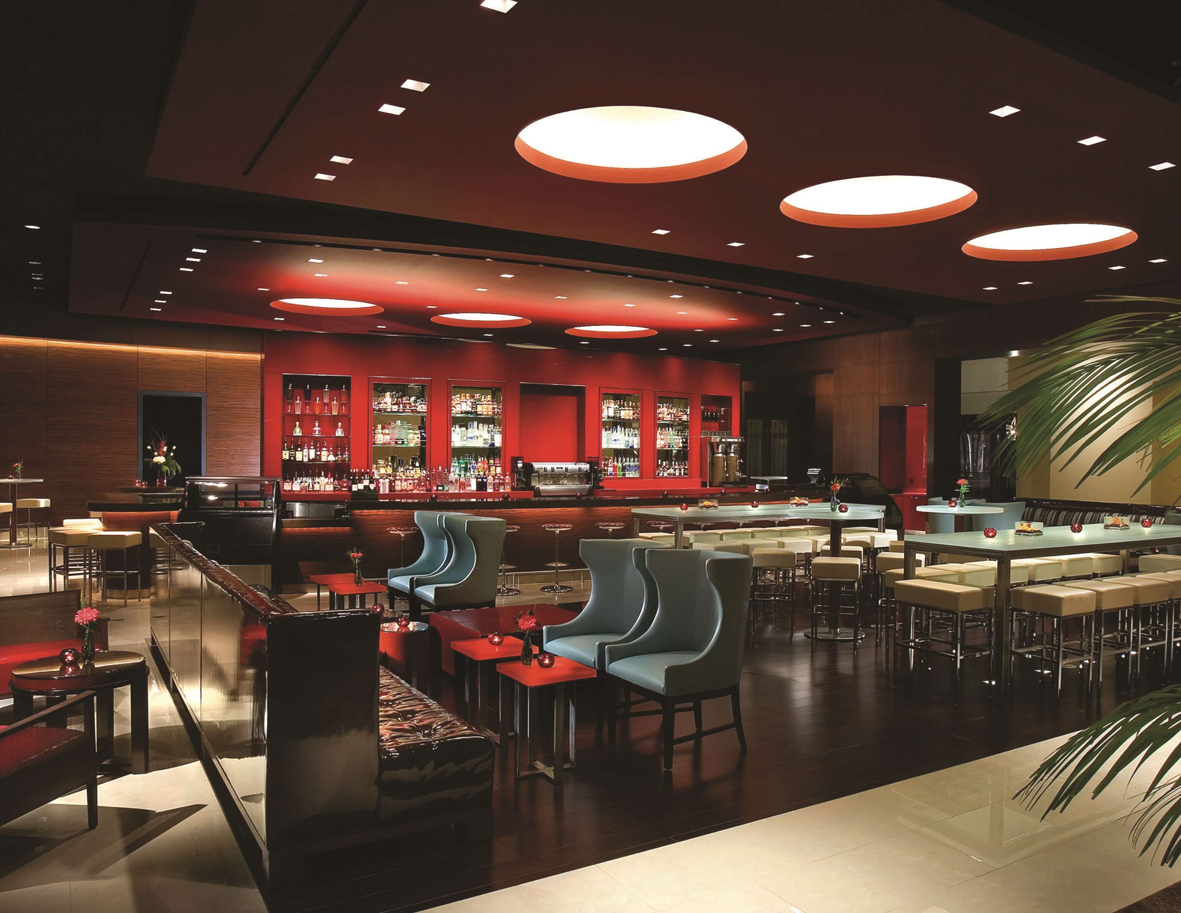 A modern bar area with seating and a bar counter, featuring a red and black color scheme and circular ceiling lights.