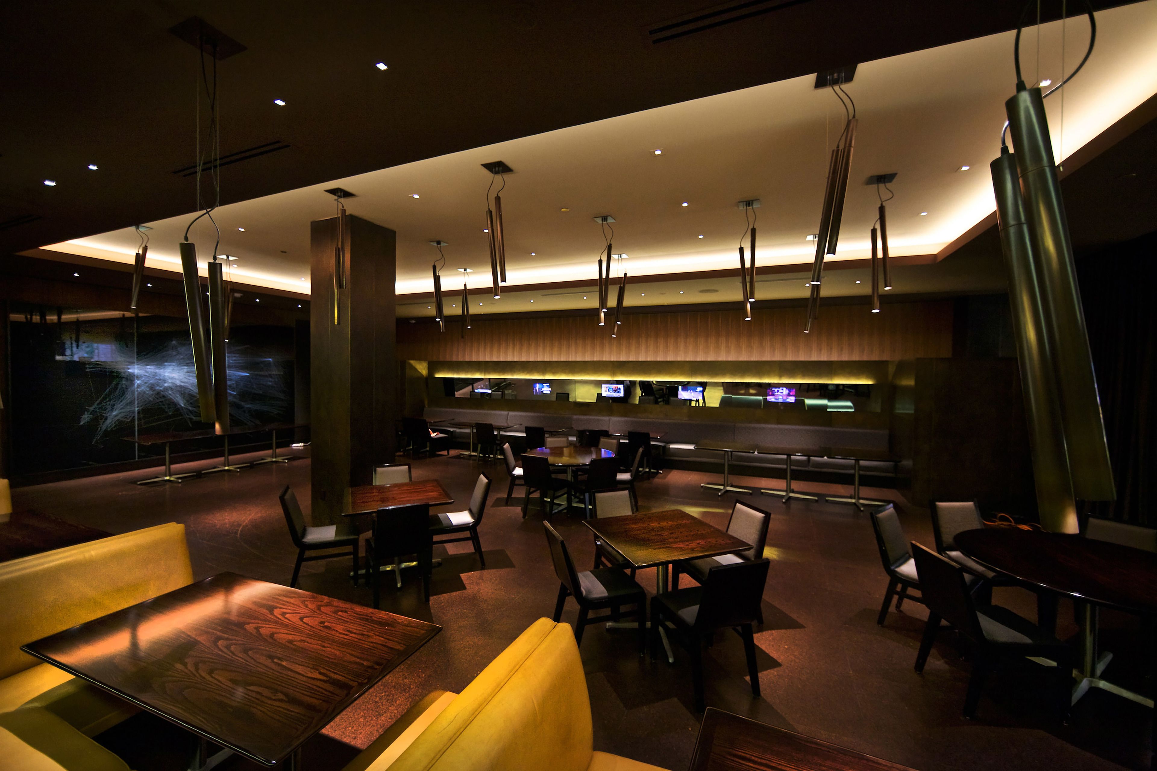 A modern restaurant with a bar area, multiple seating options including booths and tables, and a contemporary design with hanging lights.
