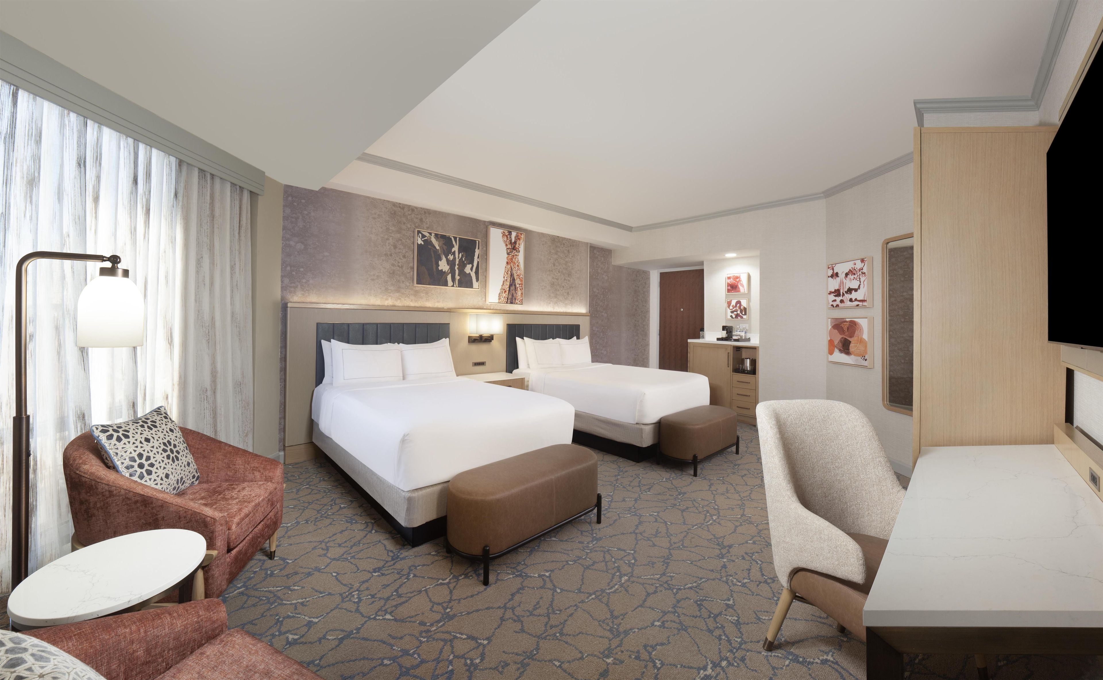 A hotel room with two beds, a sofa, a chair, a desk, and a TV.