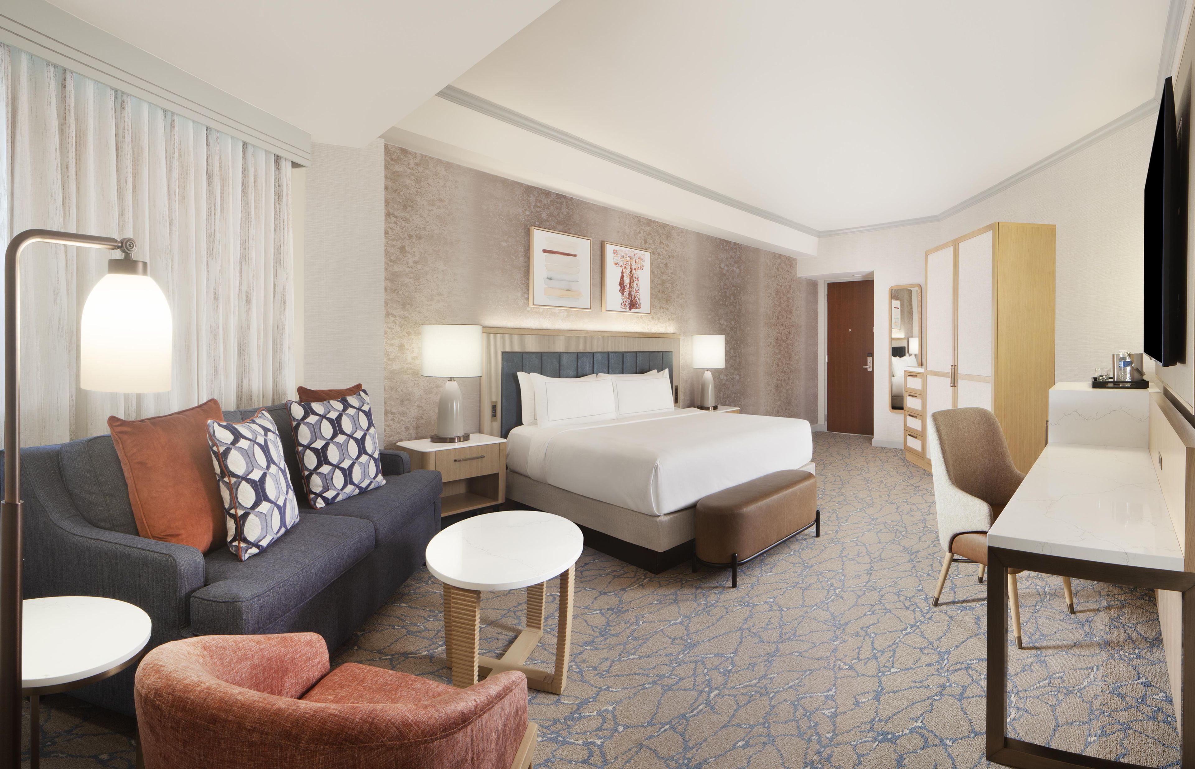 A hotel room with a bed, a sofa, a desk, a chair, and a small table.