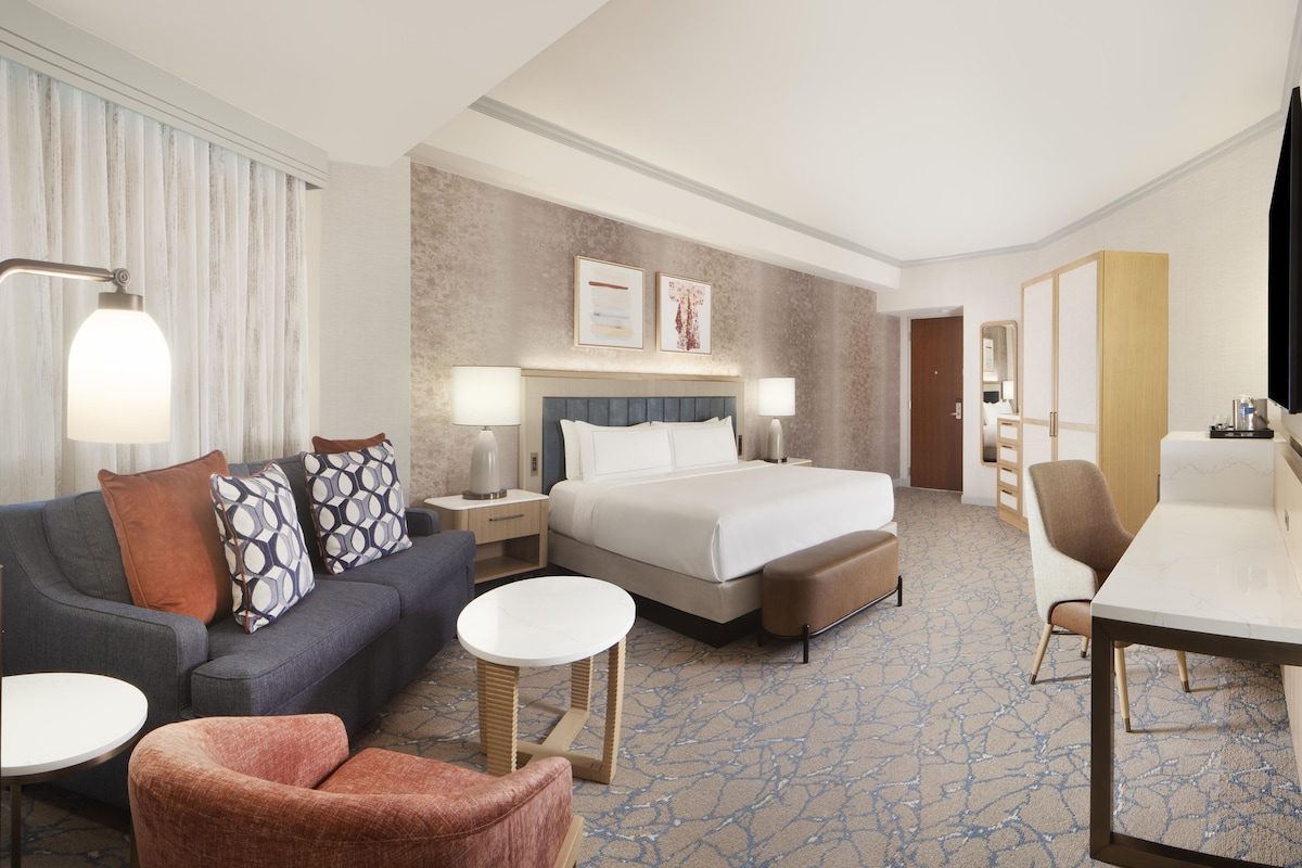 A hotel room with a bed, a sofa, a desk, a chair, and a small table.