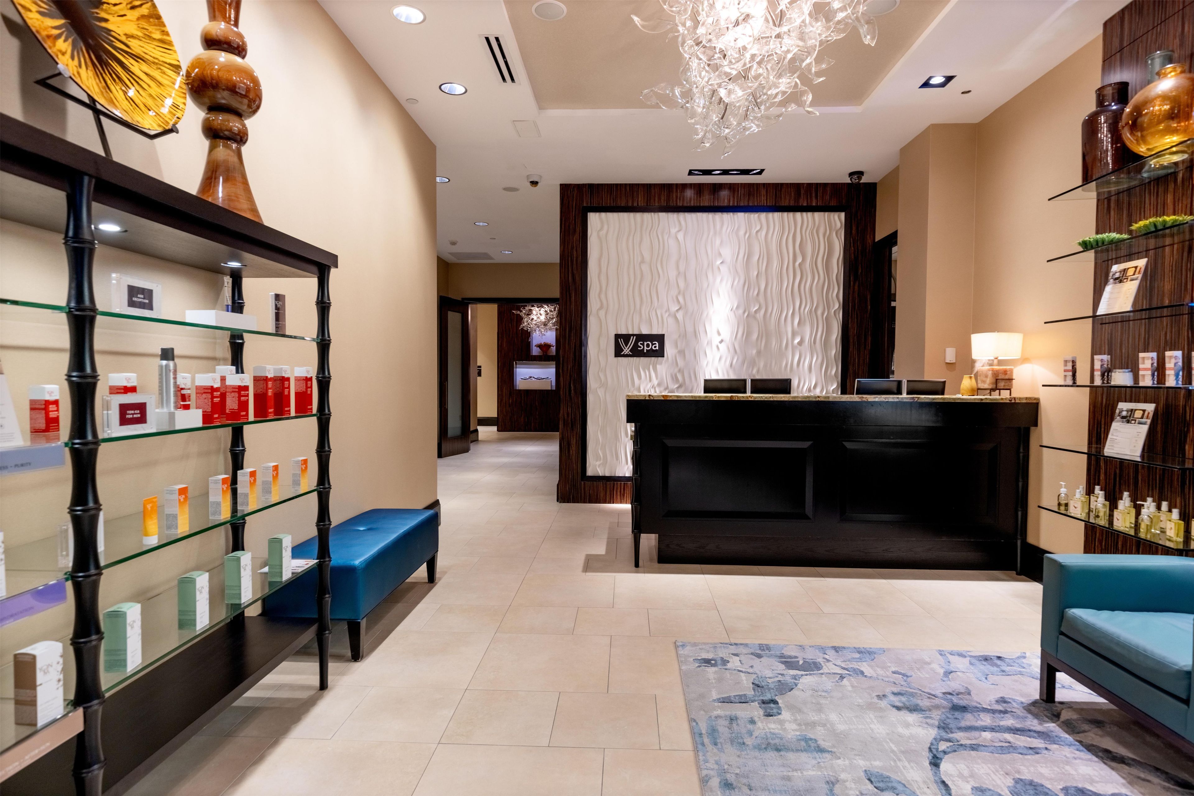 A hotel lobby with a reception desk, a blue bench, and shelves with toiletries.