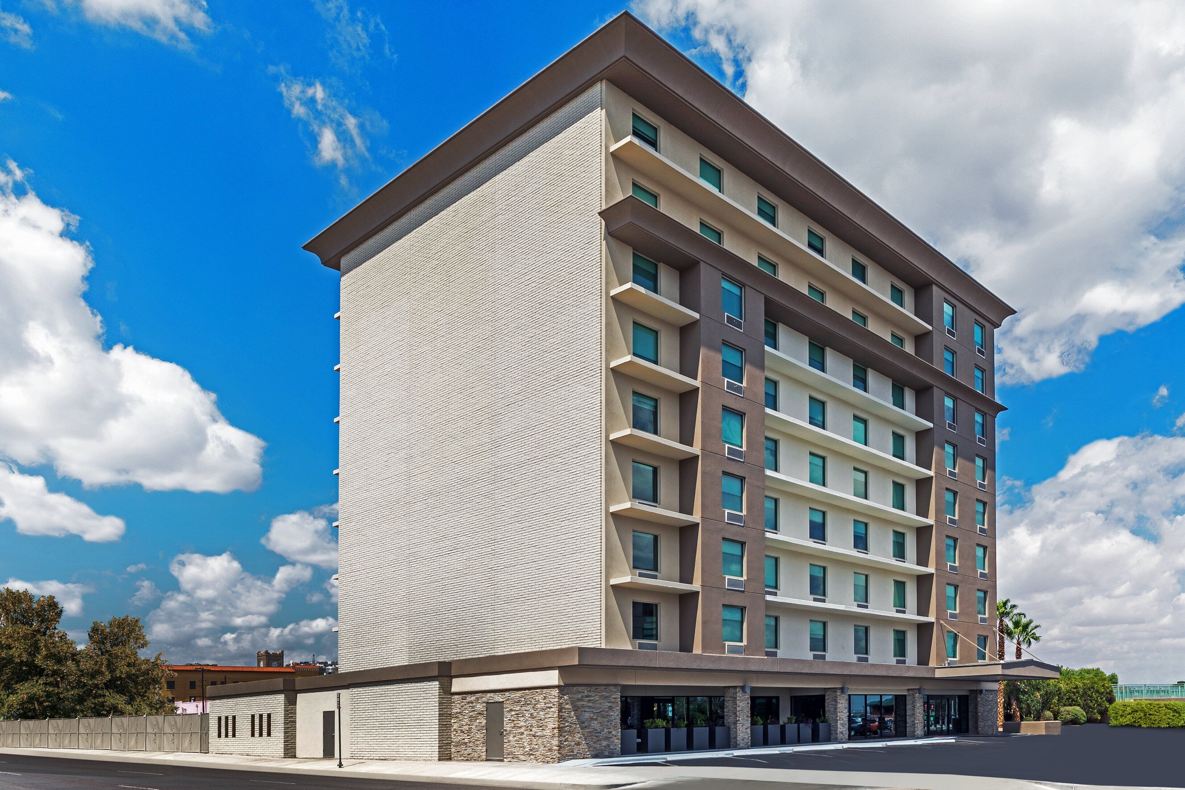 Un hôtel à plusieurs étages, doté d’un design moderne, avec un toit plat et une façade aux couleurs variées, dans des tons de beige et de brun.