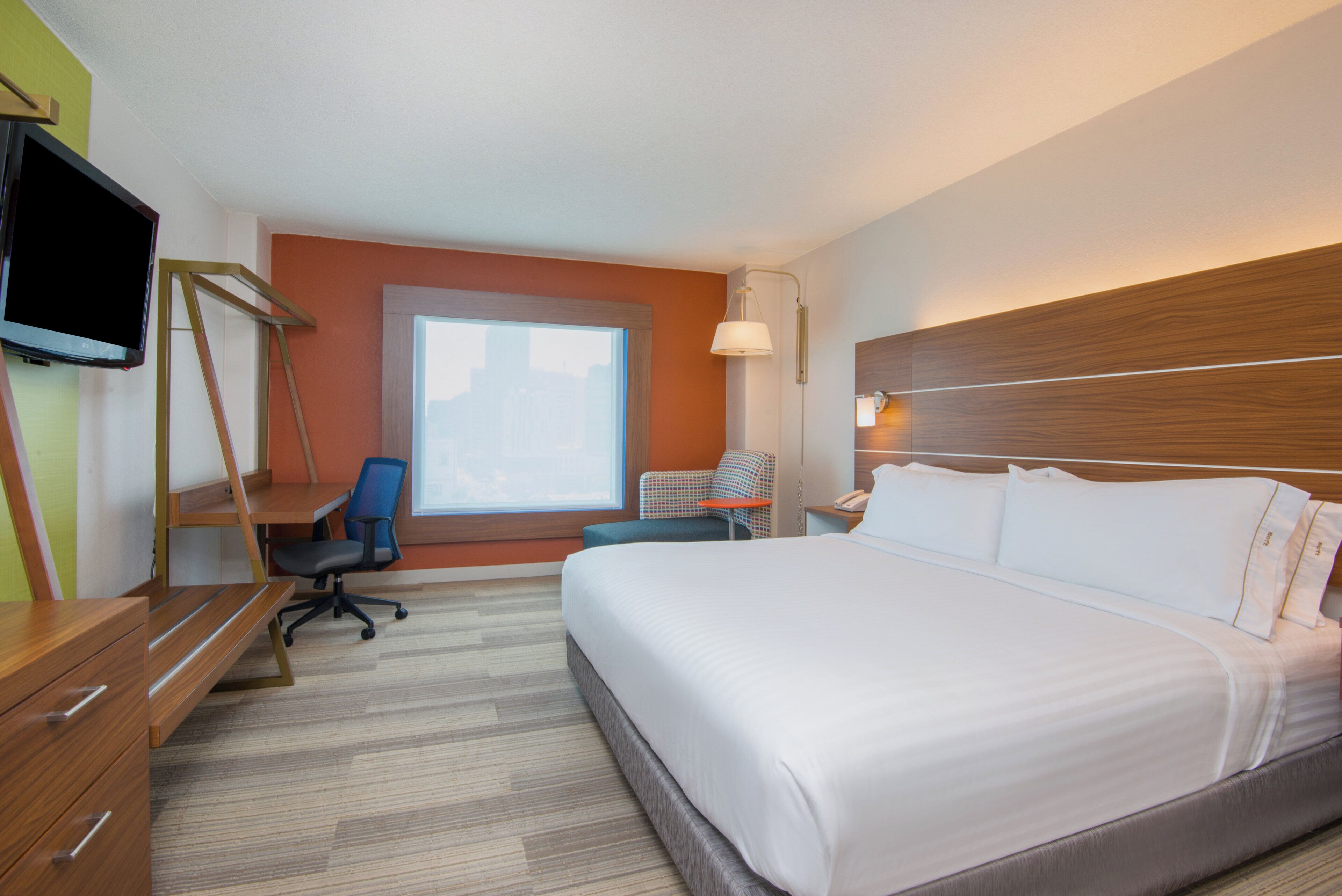 A hotel room with a bed, desk, chair, TV, and a window.