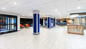 A spacious lobby with a modern design, featuring a light-colored tiled floor, blue and white pillars, and orange seating areas.