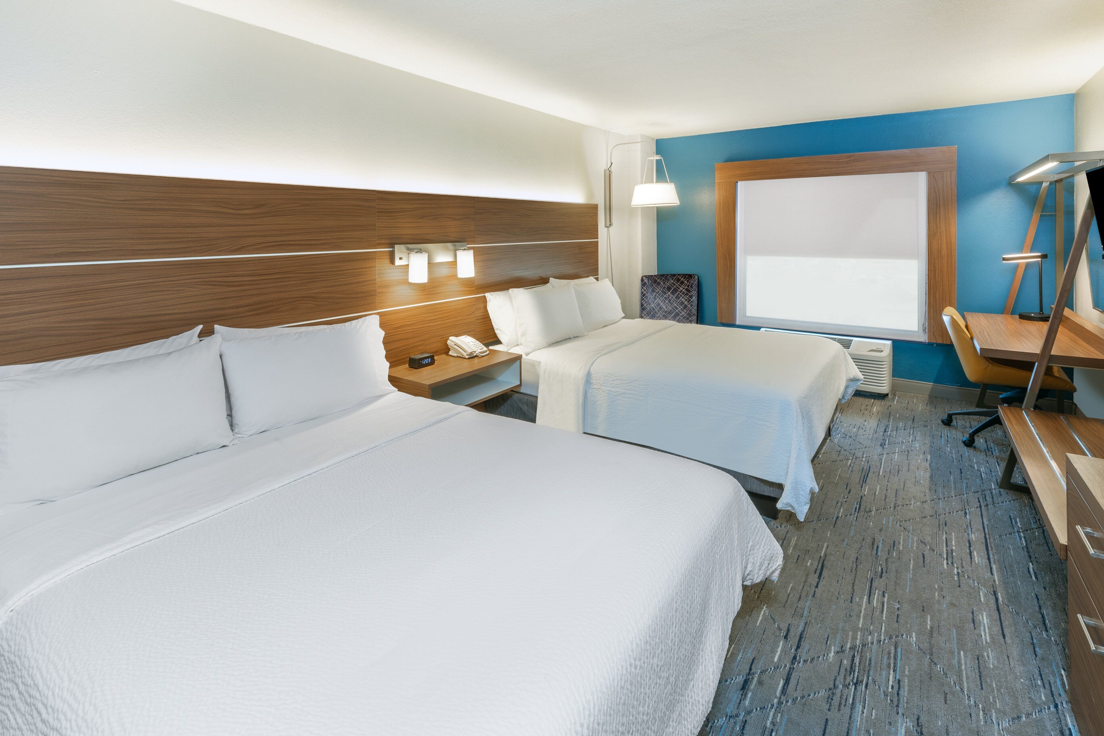 A hotel room with two beds, a desk, a chair, and a large window.