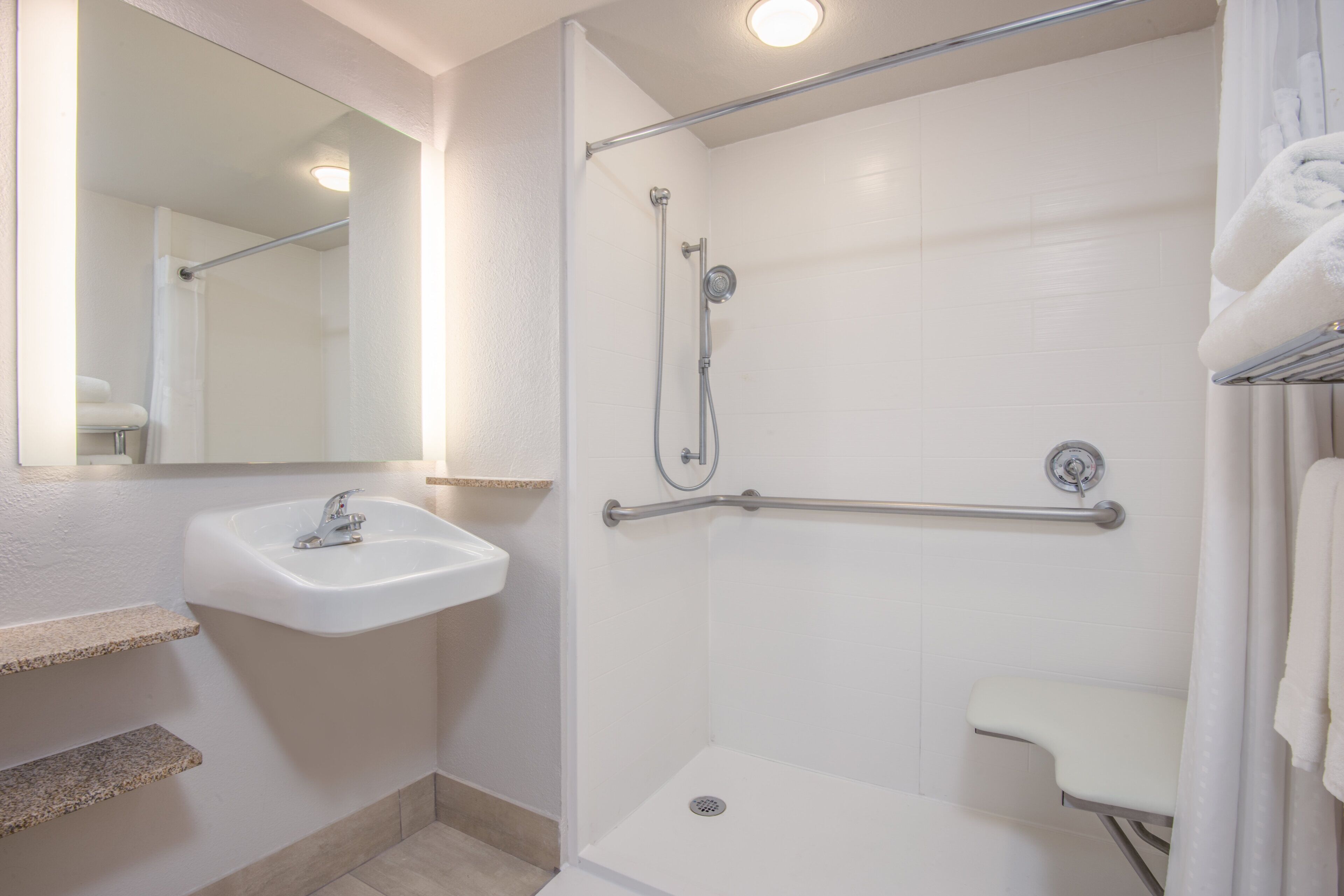 A bathroom with a white sink, a shower with a grab bar, and a mirror.