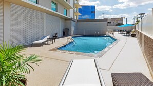 A rooftop pool area with a blue pool, lounge chairs, and a potted plant.