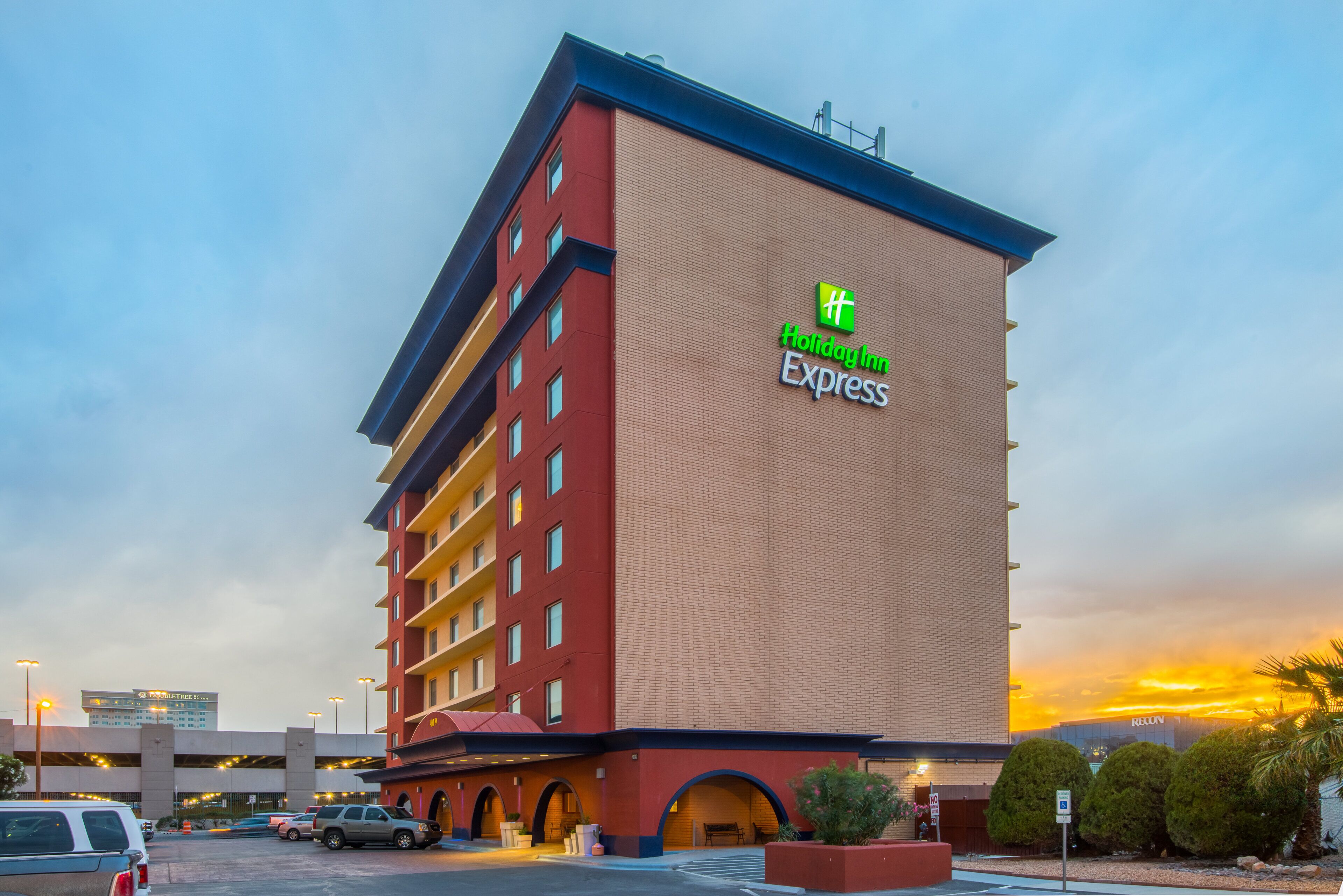 A Holiday Inn Express hotel with a red and beige facade, multiple floors, and a parking lot in the foreground.