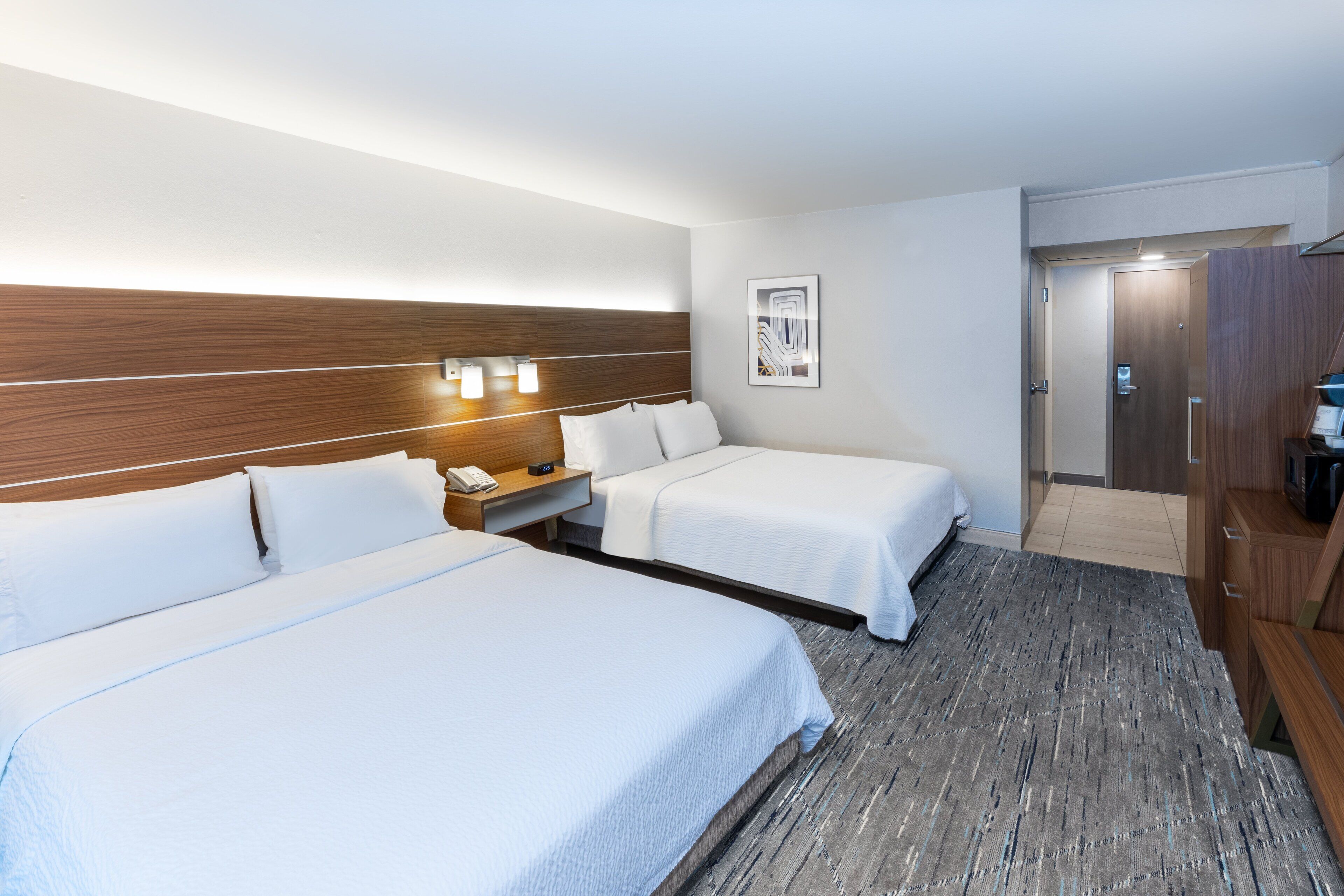 A hotel room with two beds, a wooden headboard, bedside lamps, a framed picture, and a wardrobe.