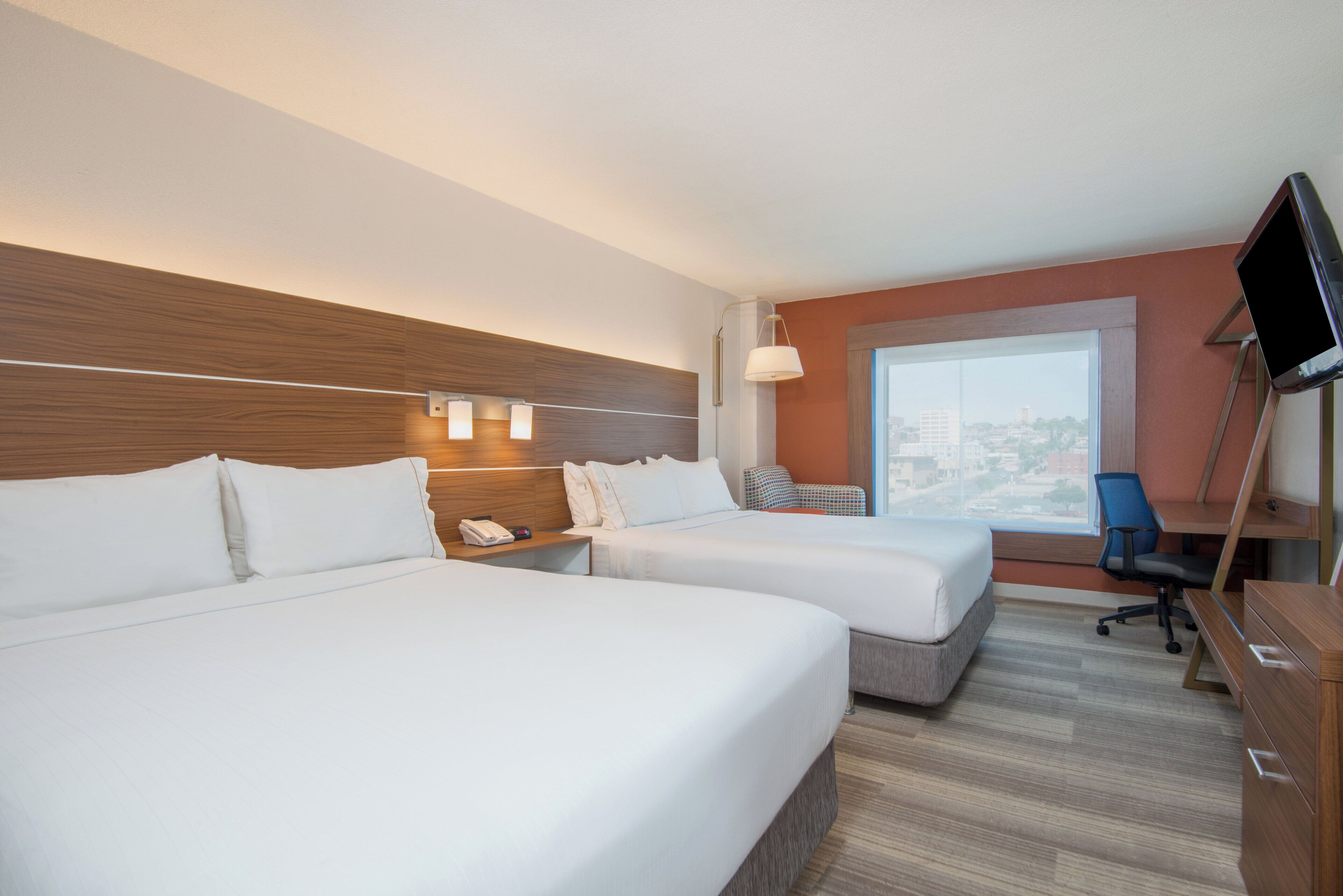 Une chambre d’hôtel avec deux lits, un bureau, une chaise, une télévision et une fenêtre donnant sur la ville.