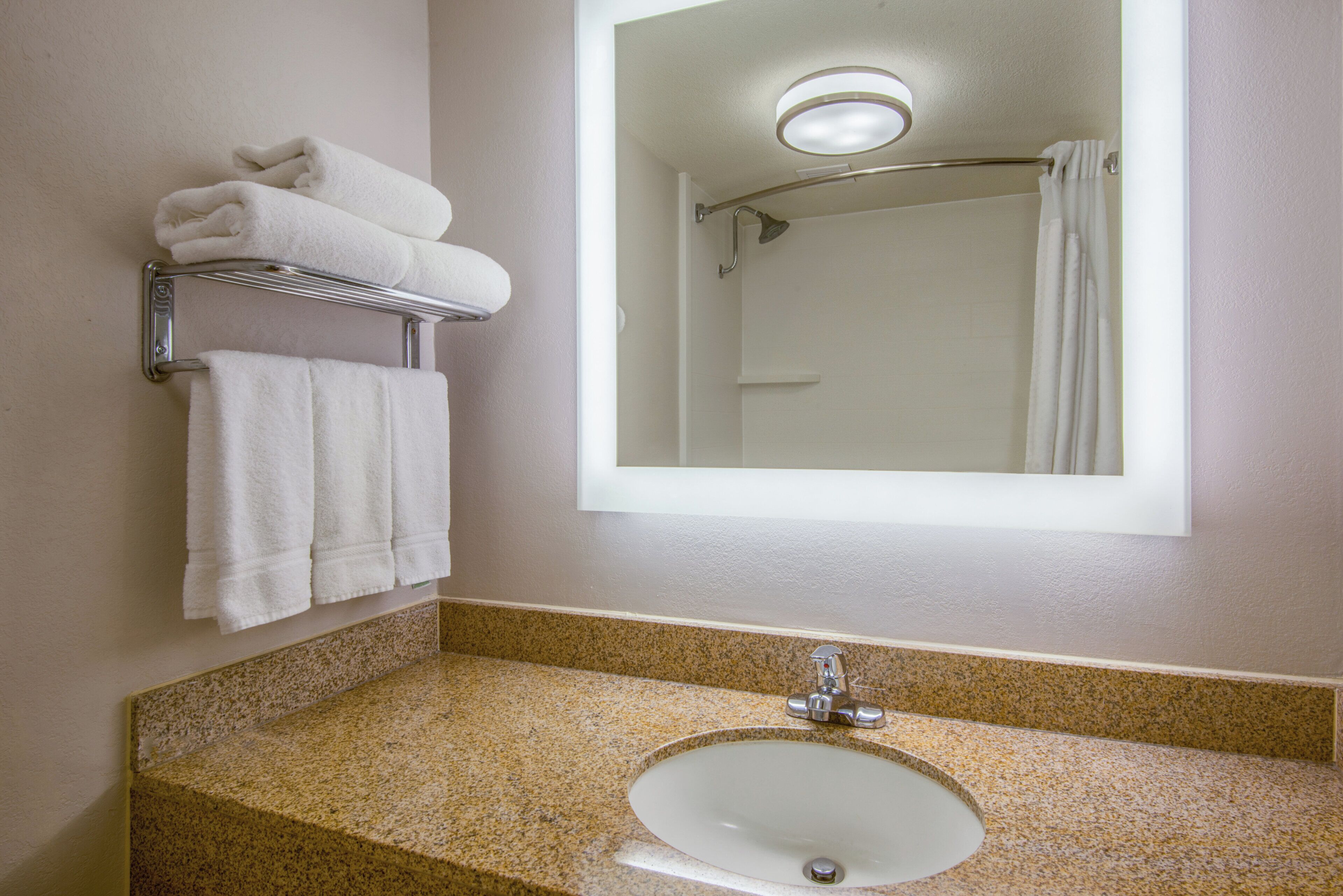 A bathroom with a sink, mirror, towel rack, and shower.