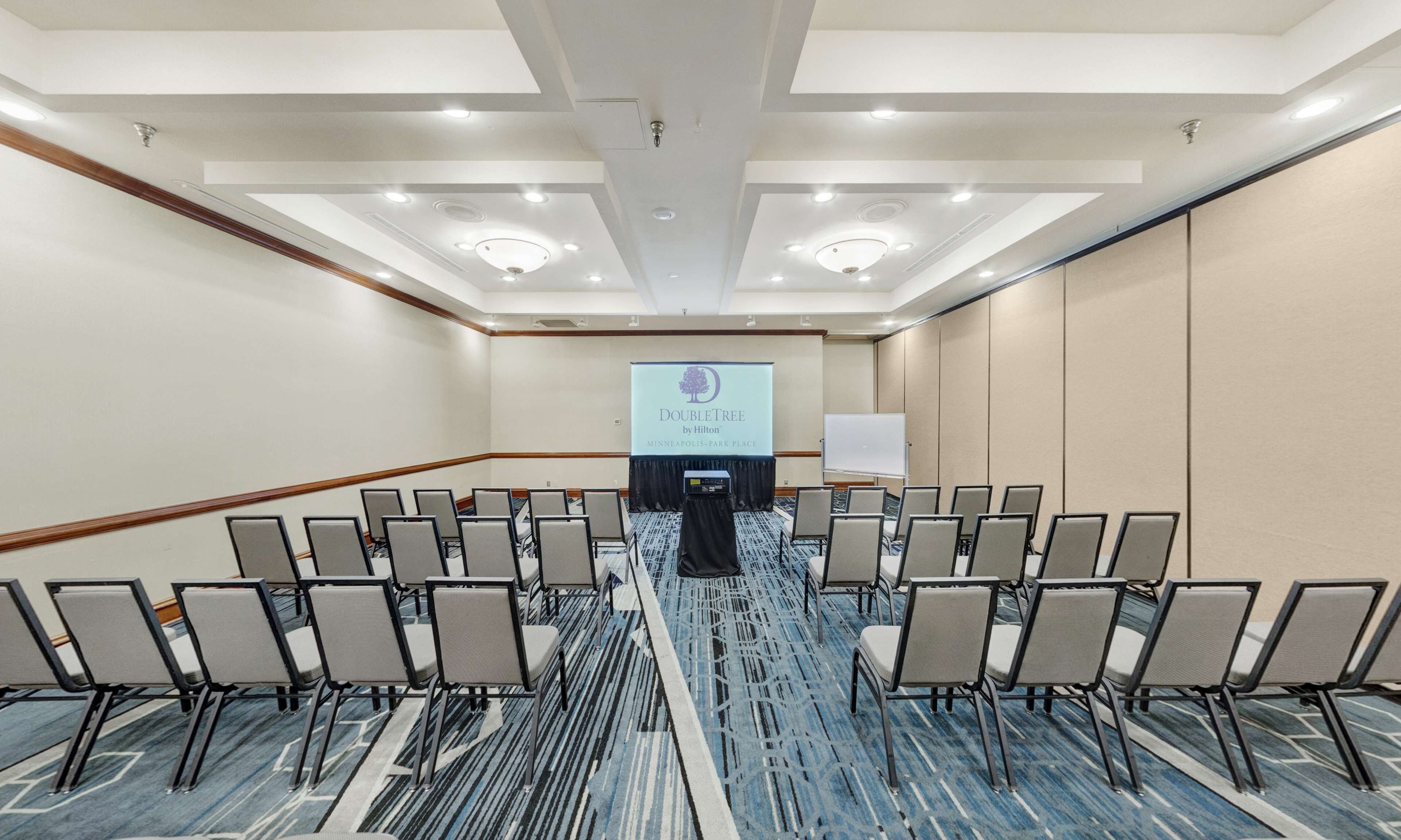 A conference room with rows of chairs, a podium, and a presentation screen at the front.