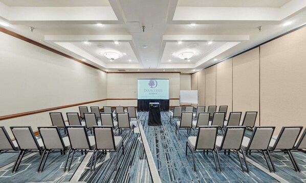 A conference room with rows of chairs, a podium, and a presentation screen at the front. - DoubleTree by Hilton Minneapolis - Park Place (St. Louis Park)