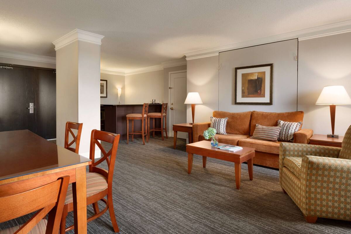 Una habitación de hotel con comedor, un sofá, una mesa de centro y una lámpara.