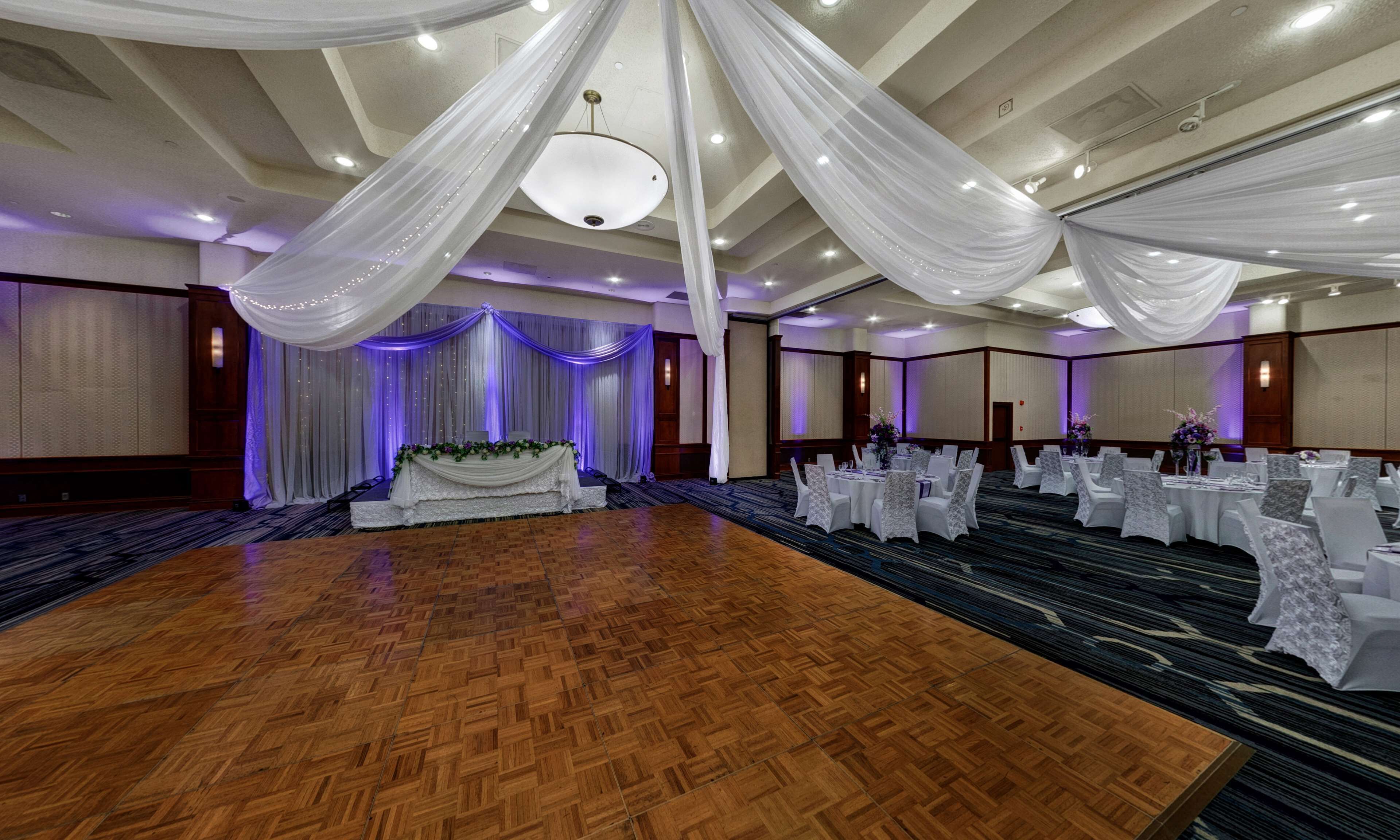 A large ballroom with a wooden dance floor, white draped ceilings, and tables set for a formal event.