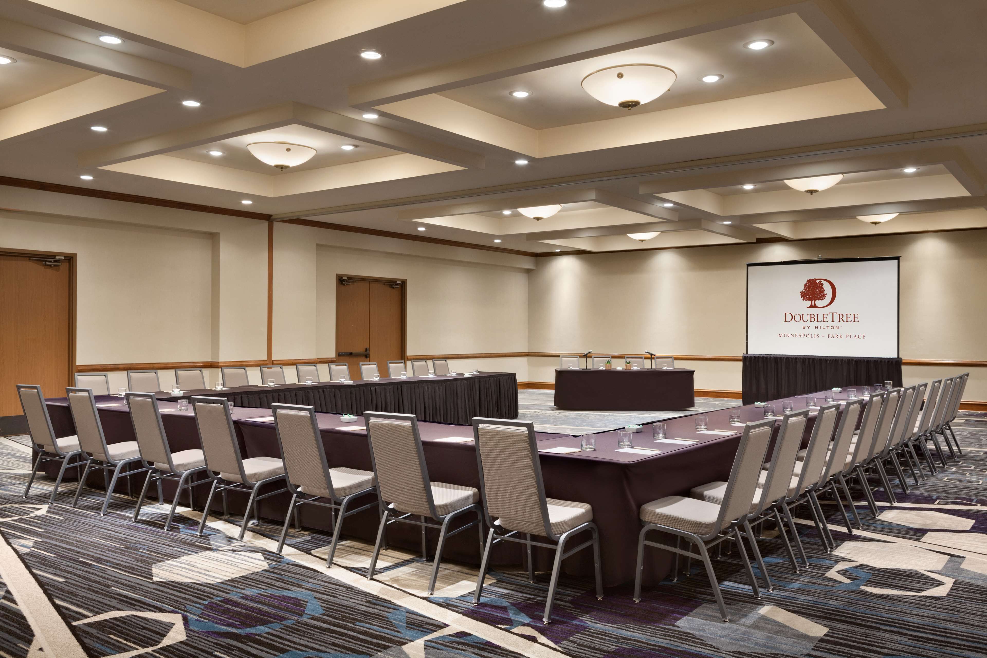 Un salón de conferencias con una larga mesa y sillas, un atril y una pantalla mostrando el logotipo de DoubleTree.