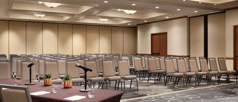 A conference room with rows of chairs, a table with a microphone, and a carpeted floor.