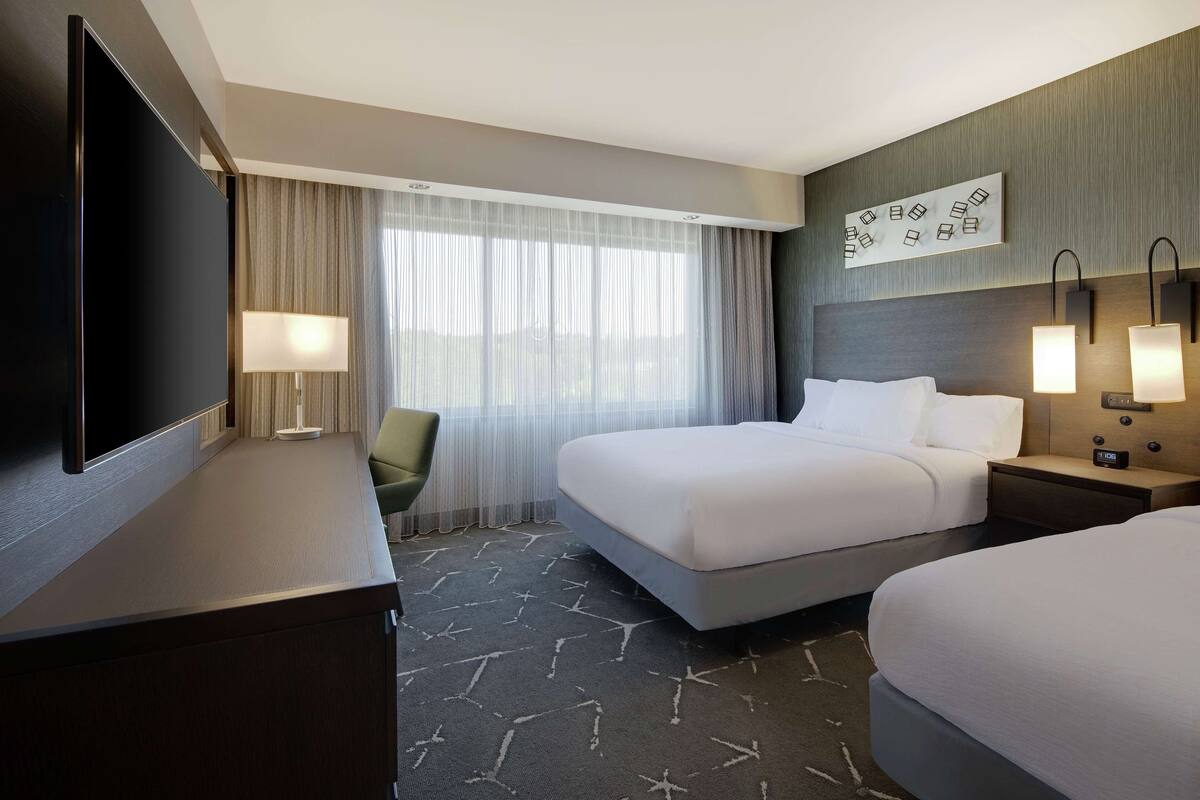 A hotel room with a large bed, a desk, a chair, a TV, and a wall-mounted artwork.