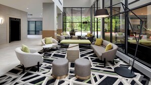Un hall d’entrée moderne, doté d’un tapis aux motifs géométriques, de meubles contemporains et de grandes fenêtres offrant une vue sur la verdure environnante.