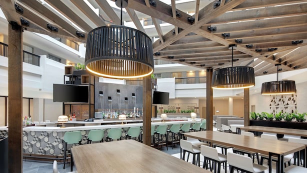 Un vaste espace intérieur comprenant plusieurs tables et chaises, un bar avec un comptoir et des sièges, ainsi qu’un plafond haut avec des poutres apparentes.