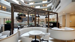 Un espace intérieur moderne doté d’une table ronde centrale entourée de chaises blanches, d’un coin salon blanc aux lignes courbes et d’une mezzanine avec des balcons.