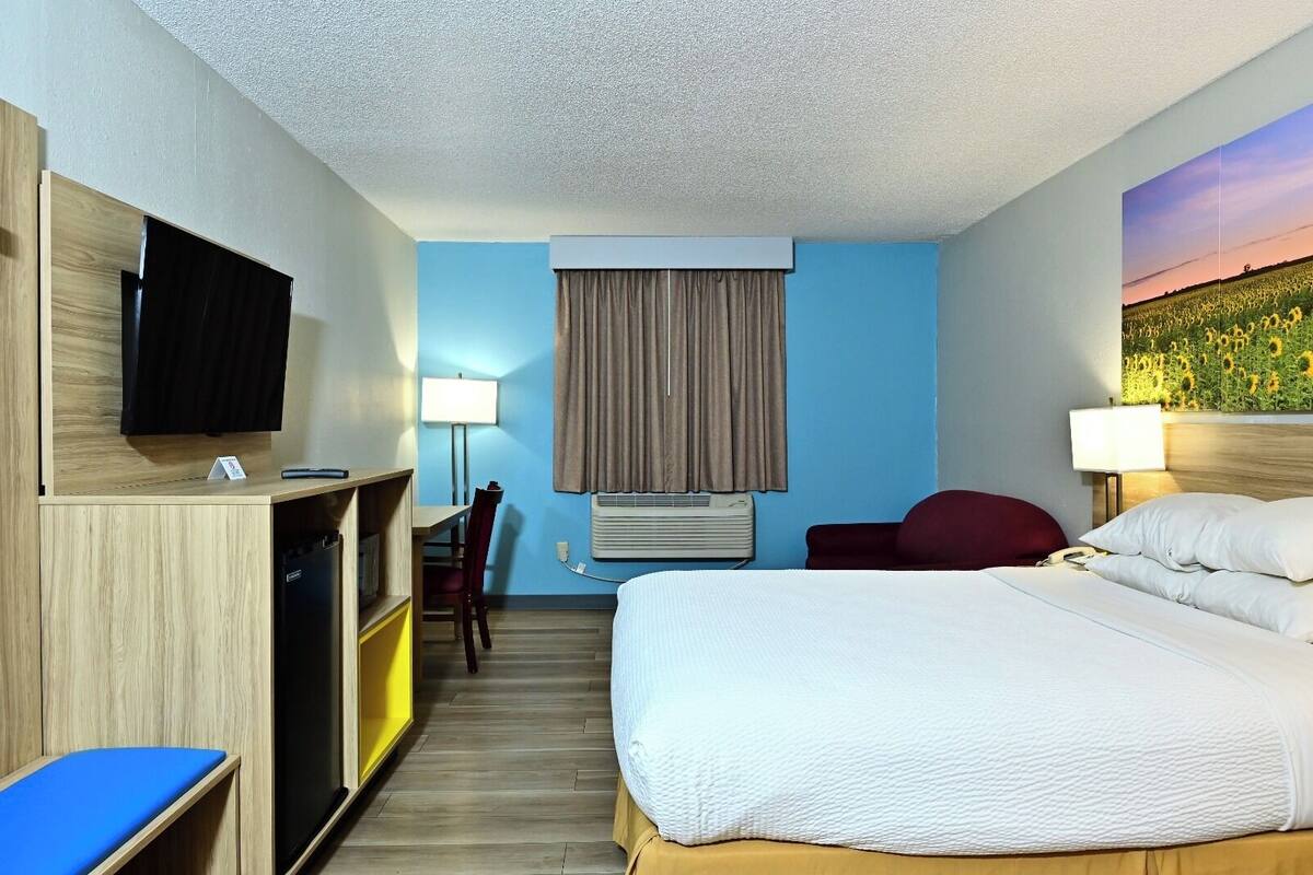Une chambre d’hôtel équipée d’un lit, d’un bureau, d’une chaise, d’une télévision, d’un climatiseur et d’un tableau au mur.
