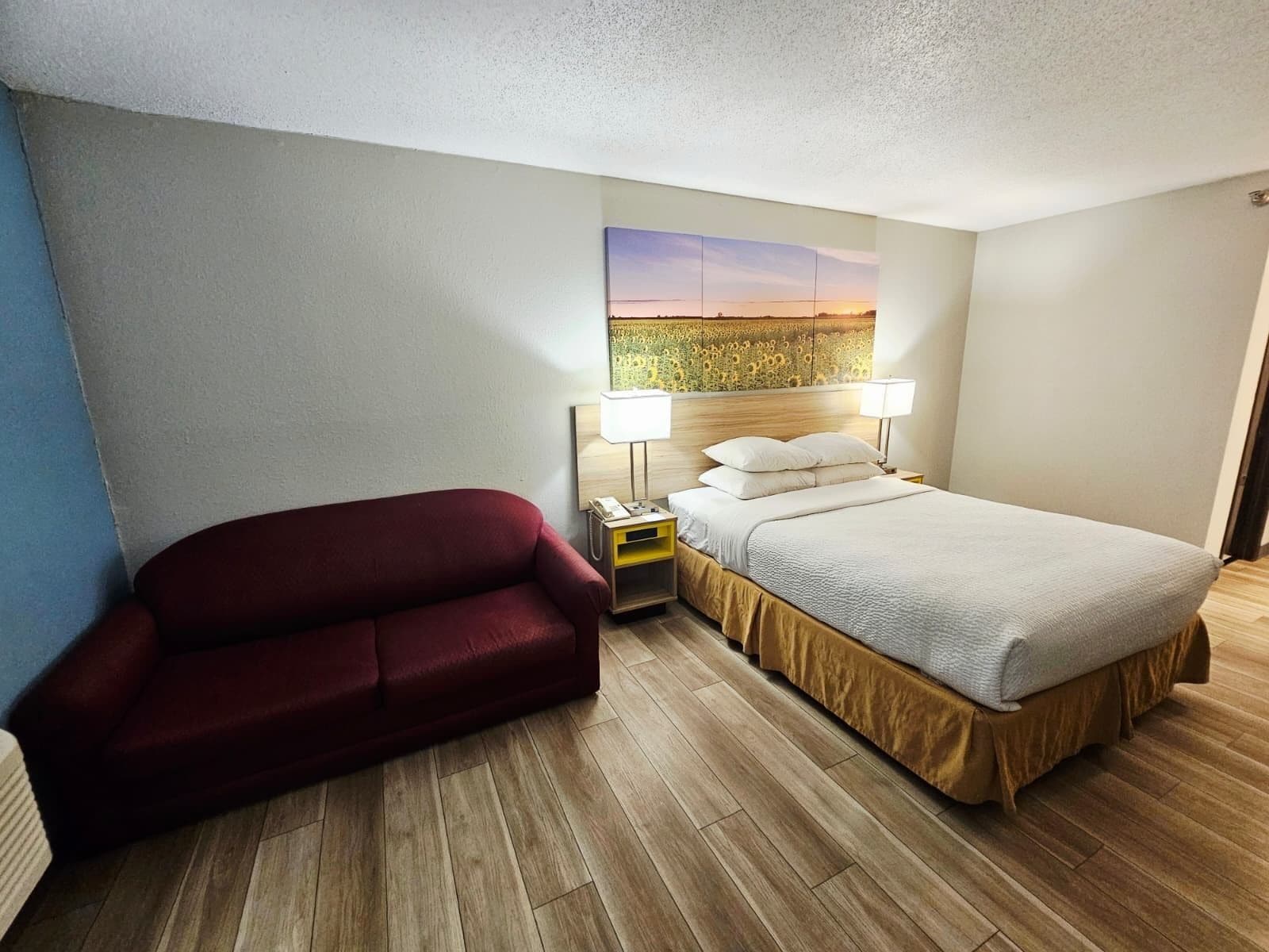 Une chambre d’hôtel avec un lit, un canapé rouge, une table de chevet avec une lampe et un tableau au mur.