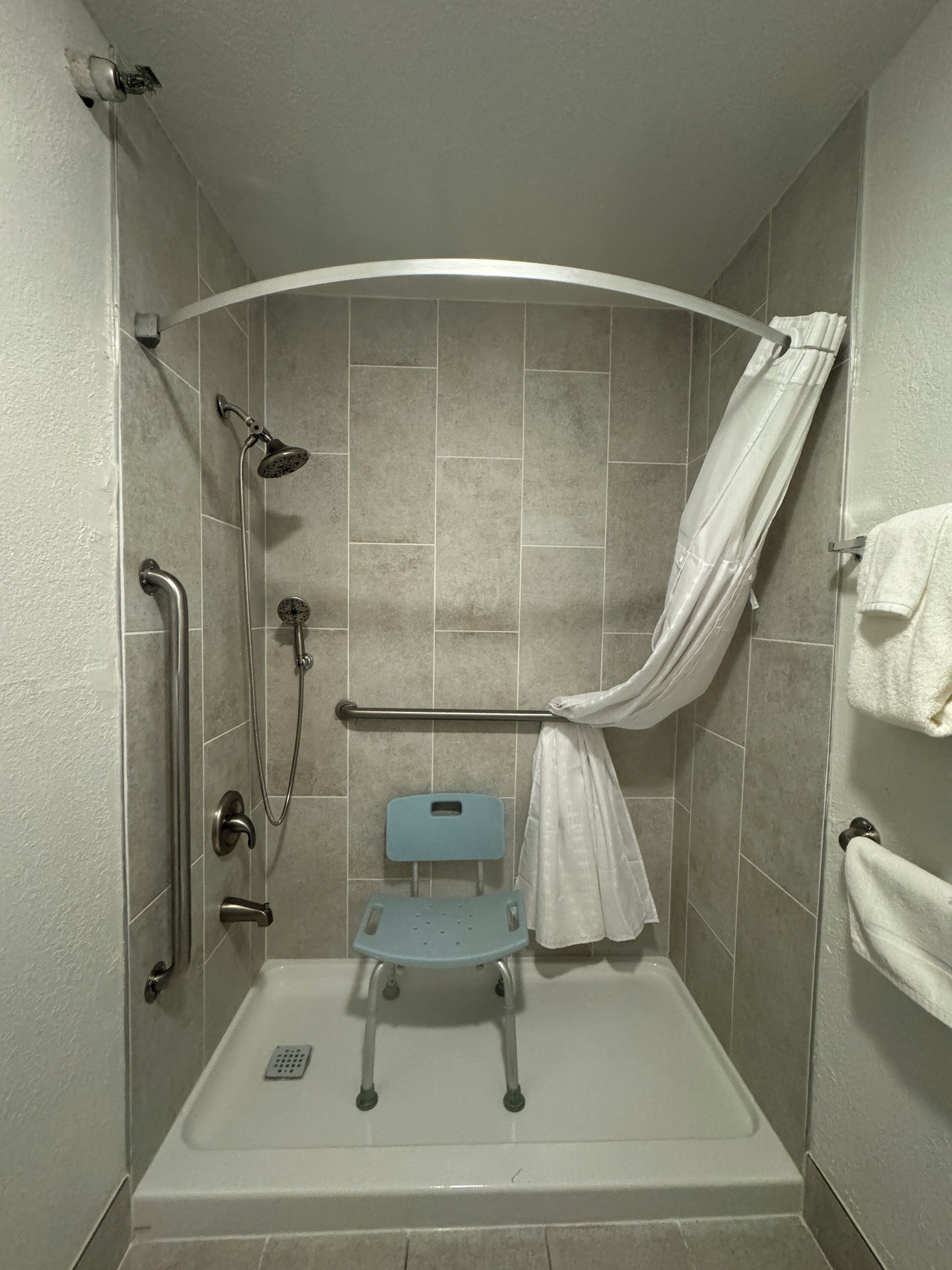 A walk-in shower with a showerhead, handheld shower, grab bars, a shower seat, and a towel rack.