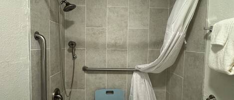 A walk-in shower with a showerhead, handheld shower, grab bars, a shower seat, and a towel rack.