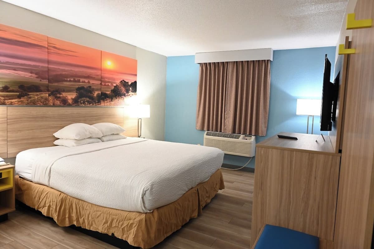 Une chambre d’hôtel équipée d’un lit, d’un bureau, d’une télévision, d’un climatiseur et ornée d’un tableau au mur.