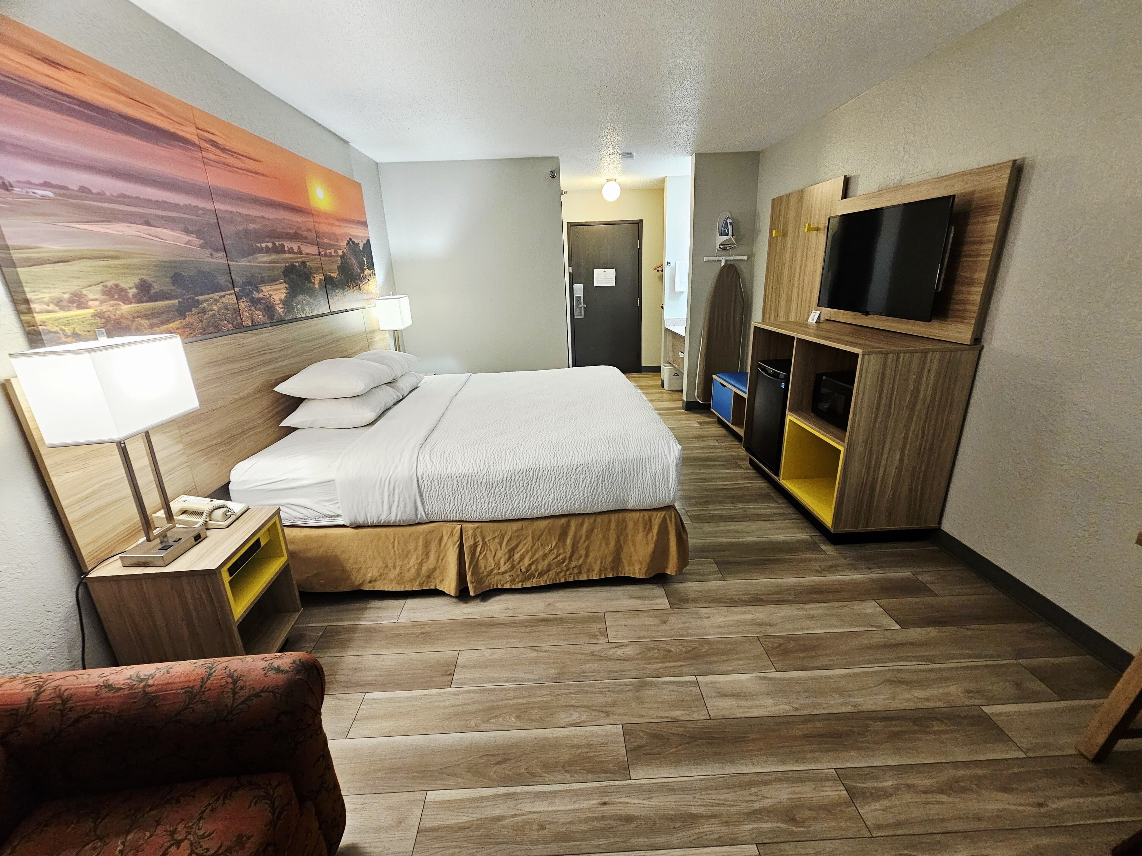 Habitación de hotel con cama, escritorio con lámpara, televisión y un cuadro en la pared.