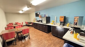 A dining area with tables and chairs, a kitchen counter with coffee machines, and a blue wall. - Days Inn by Wyndham Salina I-70 (Salina)