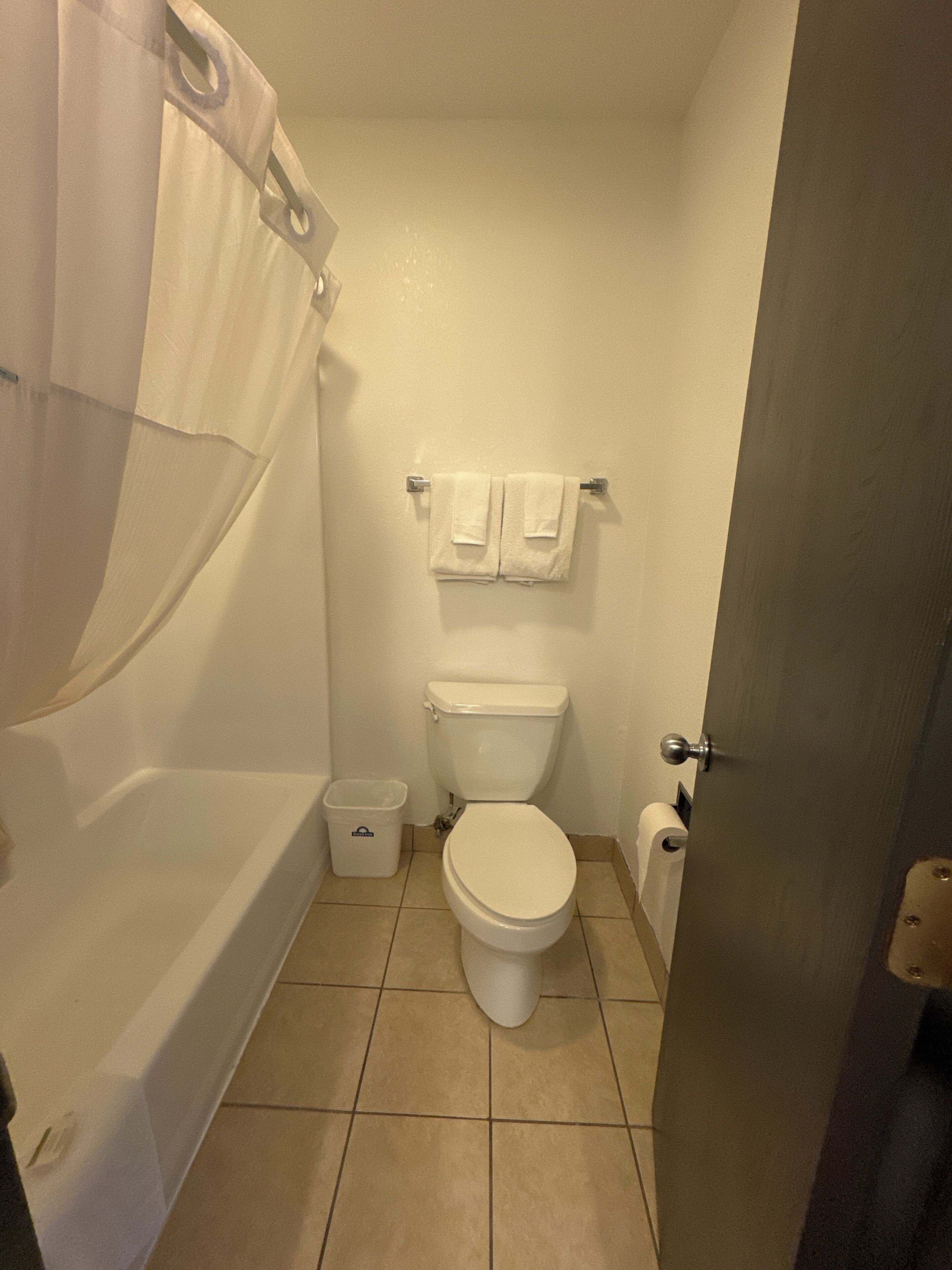 A small, clean bathroom with a toilet, a shower curtain, and a trash bin.