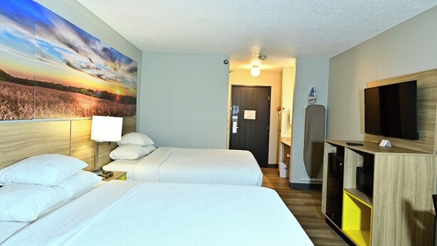 A hotel room with two beds, a TV, a desk, and a painting of a sunset. - Days Inn by Wyndham Salina I-70 (Salina)
