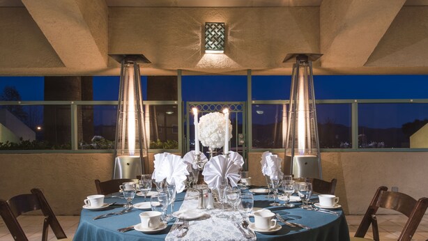 A formal dining setup with a table set for six, featuring white tablecloths, lace table runners, and candle centerpieces. - Grand Vista Hotel (Simi Valley)