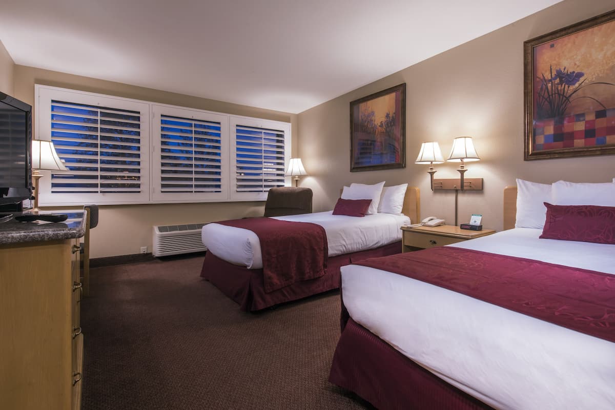 A hotel room with two beds, a desk, a chair, a TV, and a window with blinds.