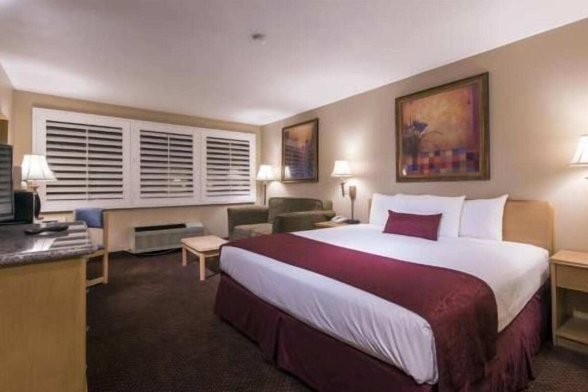 A hotel room with a large bed, two bedside tables, a desk, a chair, and a window with blinds.