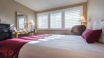Una habitación de hotel con cama, escritorio con computadora, silla, lámpara y ventana con persianas.