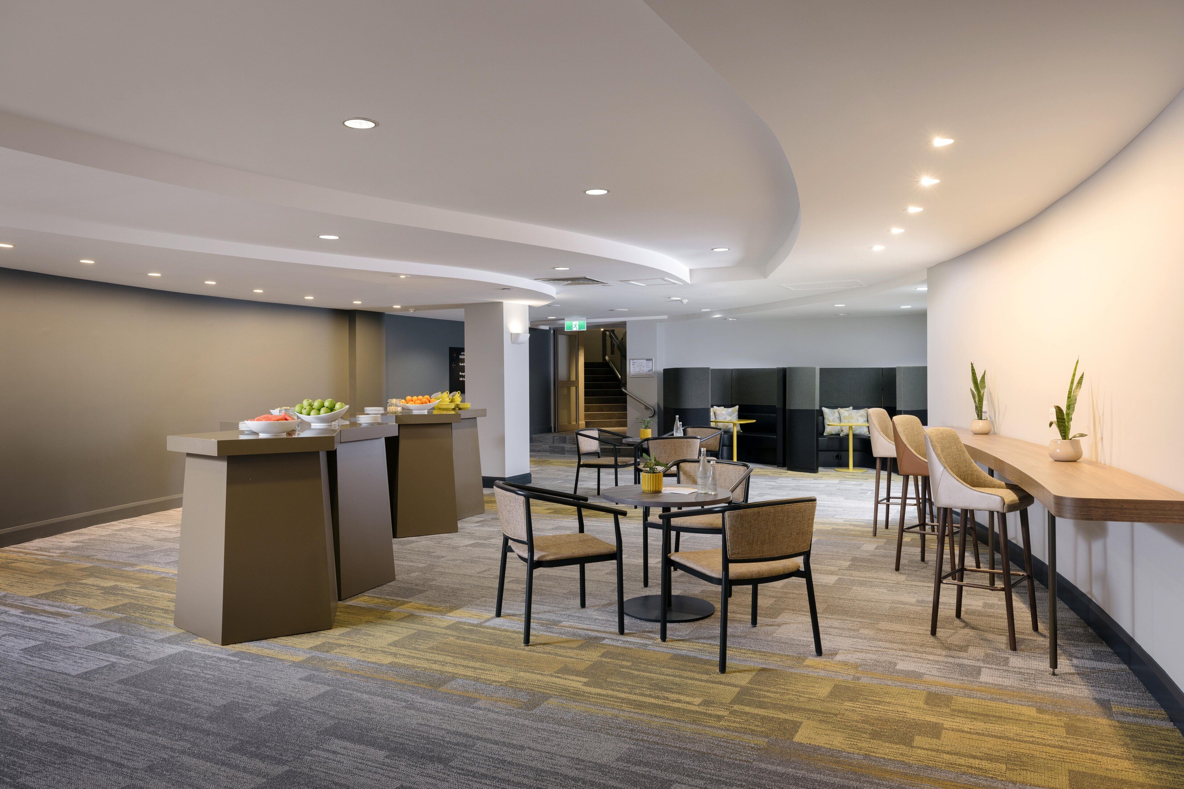 Un moderno salón con una barra central, diferentes disposiciones de asientos y una escalera al fondo.