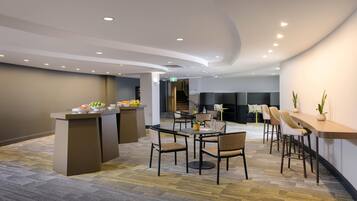 Un moderno salón con una barra central, diferentes disposiciones de asientos y una escalera al fondo.
