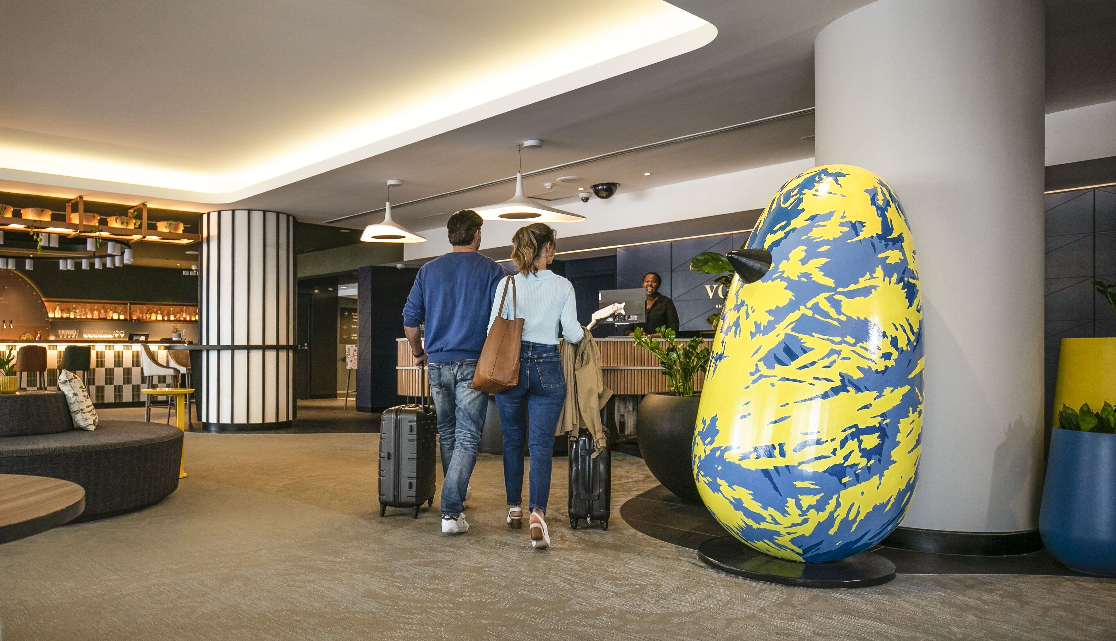 A modern lobby with a reception desk, a large globe sculpture, and a bar area with shelves of bottles.
