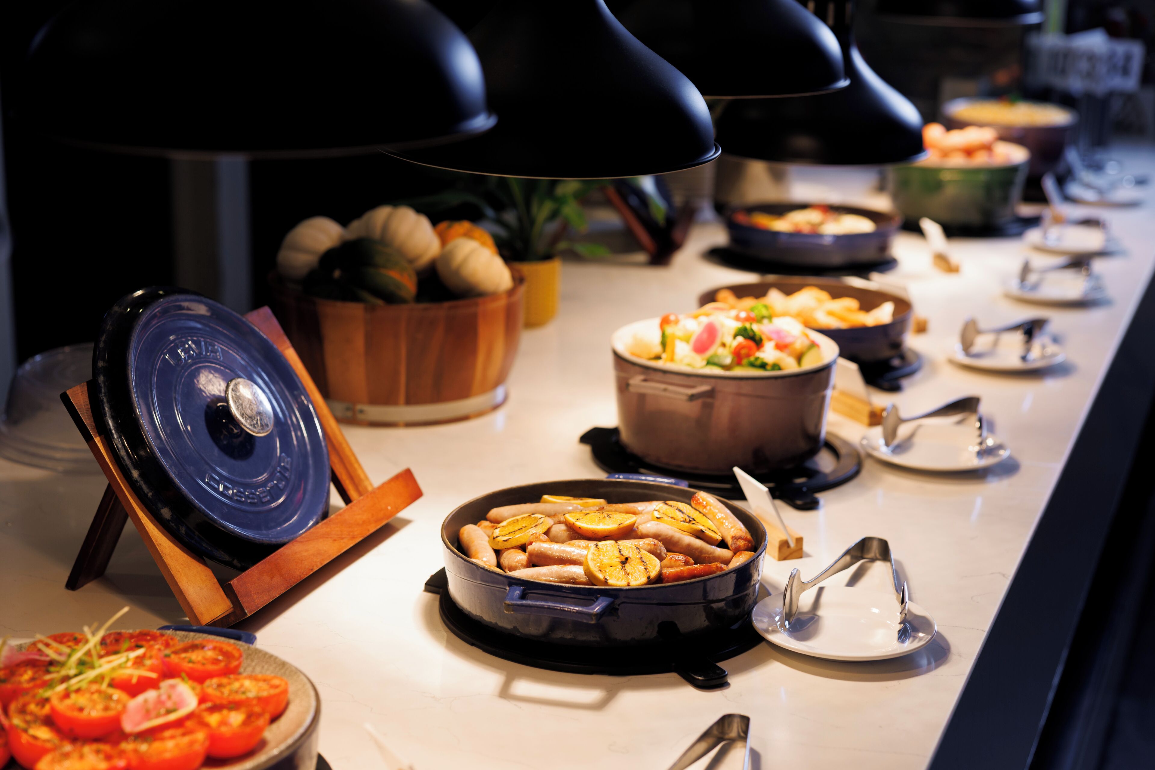 A buffet setup with various dishes, including a large pot of soup, a bowl of fruit, and a plate of sliced tomatoes.