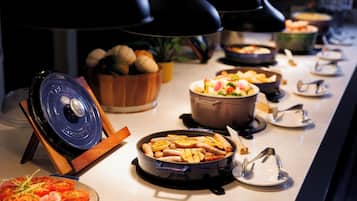 A buffet setup with various dishes, including a large pot of soup, a bowl of fruit, and a plate of sliced tomatoes.