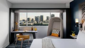 Une chambre d’hôtel avec un lit, un bureau, une chaise, une fenêtre donnant sur la ville et une lampe.