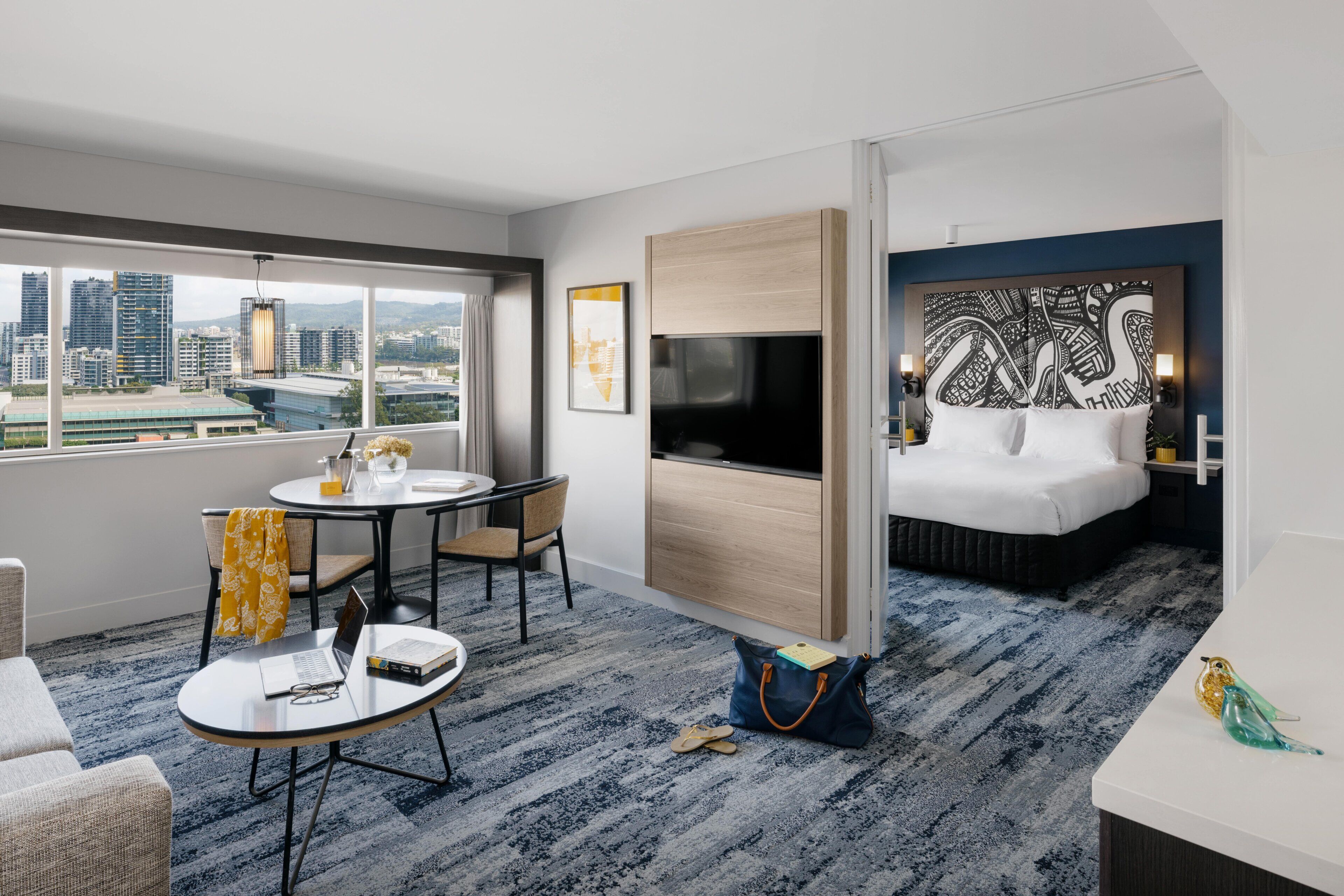 A hotel room with a city view, a dining area, a TV, a bed, and a desk.